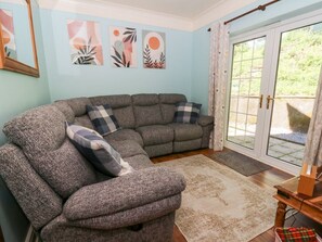 A living room with a sectional sofa, a patterned rug, and a sliding glass door leading to an outdoor area. - Ty Caredig, Pontardawe (Swansea)