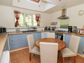 A kitchen with a round wooden table, white chairs, blue cabinets, a stove, and a microwave. - Ty Caredig, Pontardawe (Swansea)