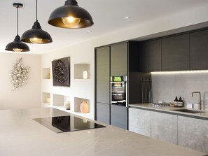 A modern kitchen with black cabinets, a built-in oven, a stainless steel sink, and pendant lighting. - Archstone House, Langho, Lancashire (Blackburn)