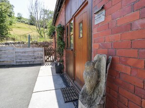 A red brick building with a wooden door, a sign reading 'Woodbeck Cottage,' and a wooden sculpture on the wall. - Woodpecker Cottage, Llangollen (Llangollen)