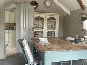 A dining area with a table set for four, a white cabinet with glass doors, and a view into the kitchen. - Butlers Loft Retreat Near Biscovey (Par)