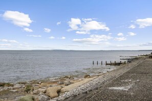 A coastal view with a pebble beach, wooden posts, and a clear sky.
