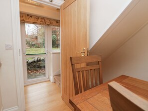 A wooden door with a brass handle, a wooden chair, and a table in a room with a window and a view of a garden. - Butterfly, in Kendal, Cumbria. (Kendal)