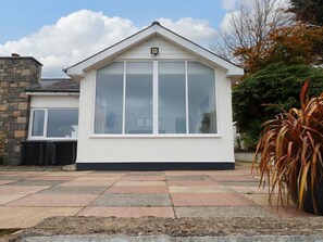 A house with a large window, a stone wall, and a tiled patio. - Summer Room, Llanbedrog, Wales (Pwllheli)