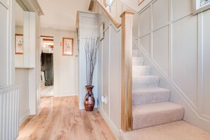 Ein Flur mit Holzboden, eine Treppe mit beigeem Teppich und eine Vase mit Zweigen.