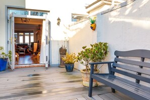 Eine geöffnete Tür, die zu einem Raum mit einer Couch, einem Tisch, einer Bank und Kübelpflanzen auf einer Holzterrasse führt.