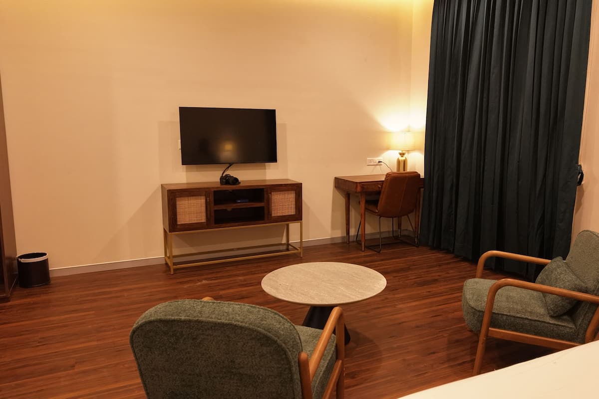 Ein Hotelzimmer mit Fernseher, Schreibtisch, zwei Stühlen, einem runden Tisch und einem Bett.