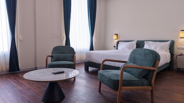 A hotel room with a bed, two armchairs, a round table, and a remote control on the table.
