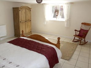 Ein Schlafzimmer mit einem Bett, einem Holzschrank, einem Schaukelstuhl und einem Fenster mit Vorhängen.