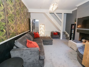 A modern living room with a sectional sofa, a fireplace, a television, and a staircase.