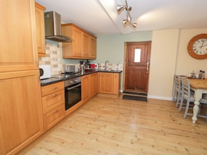 A kitchen with wooden cabinets, a stove, and a dining area with a table and chairs. - Owl Cottage, Llangollen (Llangollen)