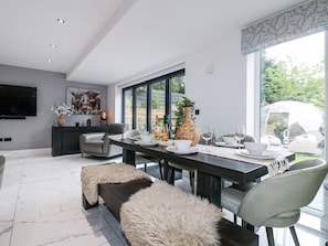 A modern dining area with a large window, a flat-screen TV, and a dining table set for four. - Rockcliffe Grange, Mansfield (Mansfield)