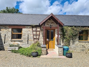 A stone building with a wooden door, a window, and a small porch area. - Puffin Cottage, Llanboidy (Whitland)