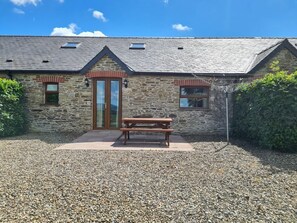 A stone building with a wooden door, a window, and a picnic table in front. - Puffin Cottage, Llanboidy (Whitland)