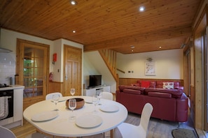 A wooden ceiling, a dining table with plates and glasses, a red leather sofa, and a television in a room with wooden walls. - Lodge 68 - Fern Gully, Chudleigh (Newton Abbot)