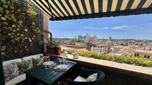 Ein Balkon mit Blick auf eine Stadtlandschaft, ein Tisch gedeckt mit Tellern und Gläsern, und ein Korbstuhl.