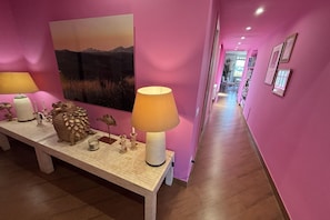 A hallway with a pink wall, a wooden bench with decorative items, a lamp, and a framed picture. - Luxury Penthouse With Amazing Views (Roma)