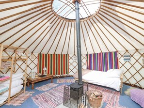 A yurt with a central stove, a bed, a wooden shelf with pillows, and colorful striped rugs. - Moonlight Retreat in Ventnor (Ventnor)