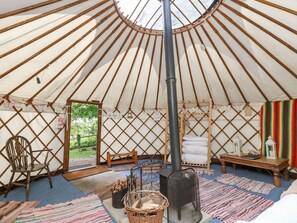 A yurt interior with a central pole, a stove, a chair, a table, and a view through the entrance. - Moonlight Retreat in Ventnor (Ventnor)