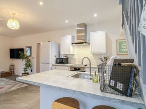 A modern kitchen with a central island, stainless steel appliances, and a hanging light fixture. - Charming The Kiln in Colmworth (Bedford)