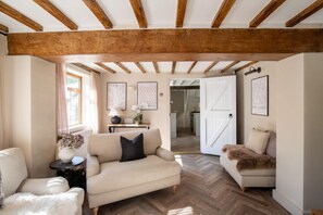 A cozy living room with a wooden ceiling, a sofa, a chair, a small table with a vase, and a door leading to another room. - Rainbow Cottage, Ormskirk (Ormskirk)