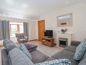 A living room with a sofa set, a television on a wooden stand, a fireplace, and a window with curtains. - Daisy Nook, Withernsea (Hull)