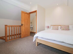 A bedroom with a wooden bed frame, a carpeted floor, a wooden door, and a bathroom visible through an open door. - Daisy Nook, Withernsea (Hull)