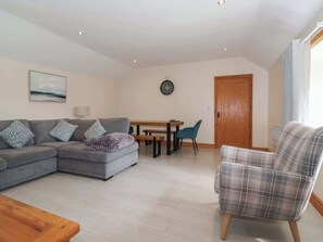 A living room with a grey sofa, a plaid armchair, a wooden dining table, and a wooden door. - Daisy Nook, Withernsea (Hull)