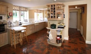 A kitchen with a central island, wooden stools, a built-in bookshelf, and a tiled floor. - Glenfarg House, Glenfarg (Glenfarg)
