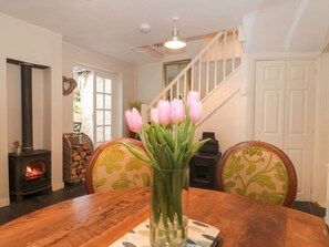 A dining area with a wooden table, chairs, a vase of flowers, a fireplace, and a staircase. - The Cottage Loaf, Wedmore (Wedmore)