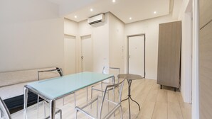 A modern room with a glass-top table, metal chairs, a small round table, a sofa, a wardrobe, and an air conditioning unit. - Roberto Flat - 10 min da Fiera di Verona (Verona)
