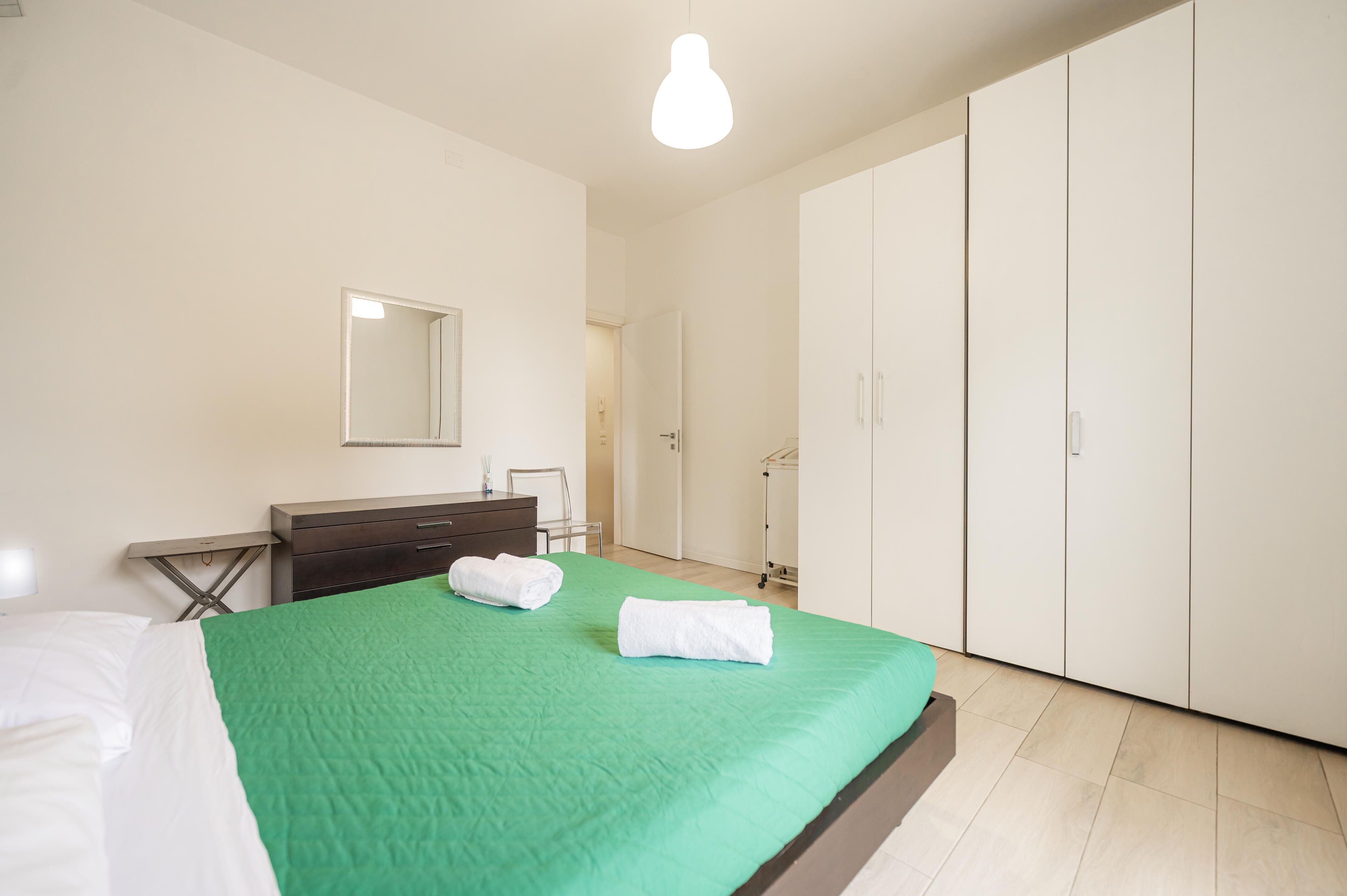 A bedroom with a bed, a dresser, a mirror, and a wardrobe.