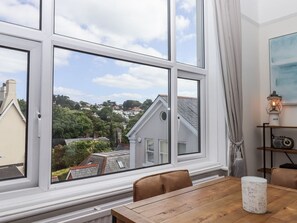 A room with a large window, a wooden table, a chair, a lamp, and a shelf with a radio. - Kinbrae Apartment, Torquay (Torquay)
