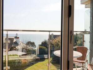 A balcony with a glass door, a wicker chair, and a table. - The Old Harbour Masters House, Fowey (Fowey)