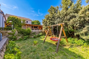 A residential property with a stone wall, a wooden swing set, and a garden with various plants. - Hidden Hill Lopar With Sauna & Jacuzzi (Lopar)