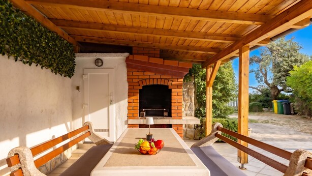 An outdoor patio with a brick fireplace, wooden benches, and a table with fruit. - Hidden Hill Lopar With Sauna & Jacuzzi (Lopar)