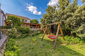 Ein Garten mit Schaukel, Steinmauer und einem Haus mit Ziegeldach.