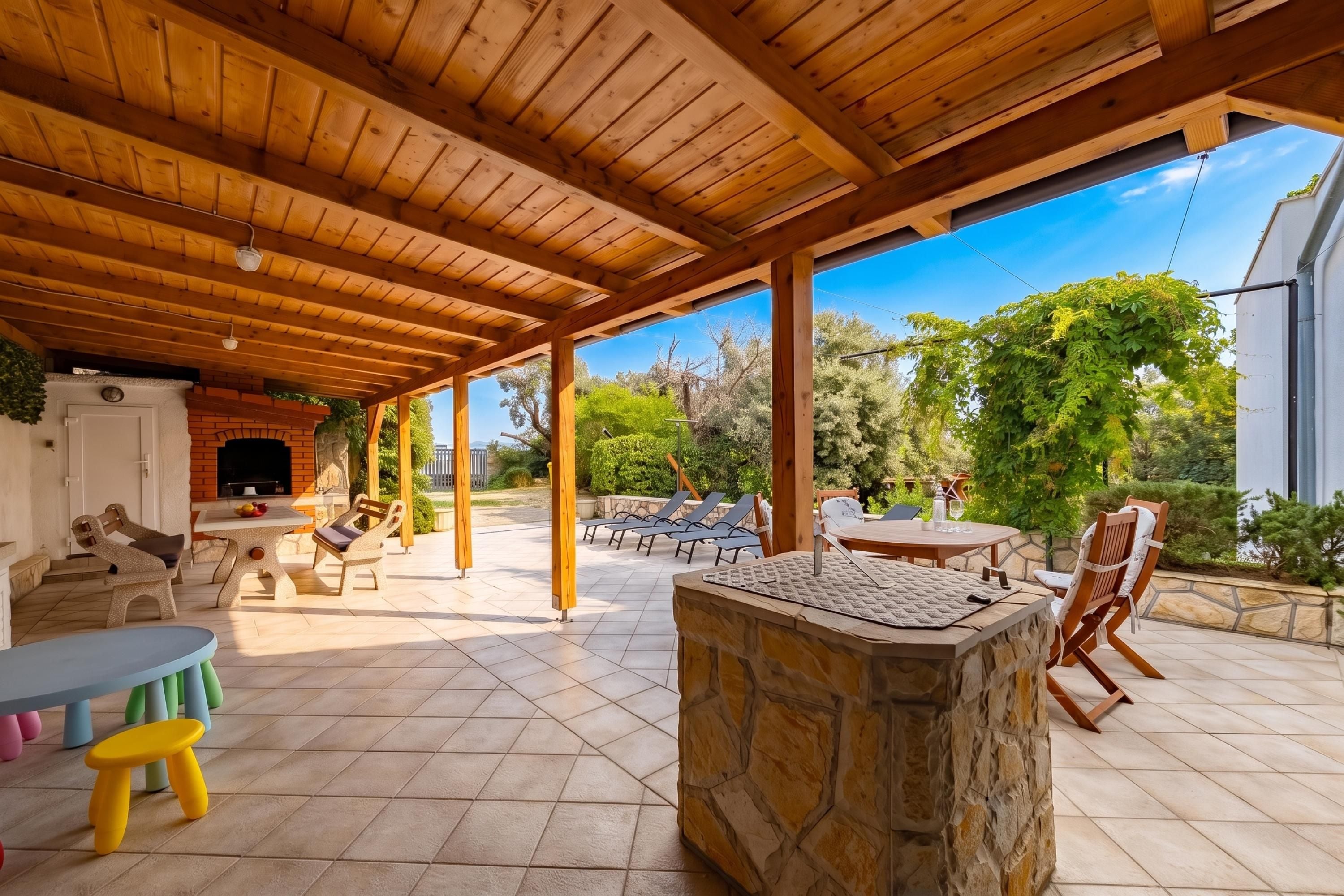 An outdoor patio with a stone fireplace, wooden ceiling, and a view of the surrounding greenery.