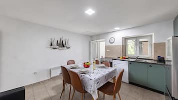 Un comedor con mesa preparada para cuatro, una cocina con electrodomésticos modernos y un reloj en la pared.