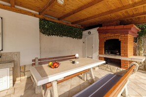 Een terras buiten met een tafel, een bank en een bakoven van baksteen.