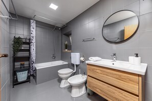 Un baño moderno con bañera, dos inodoros, un lavabo, un espejo y una ducha.