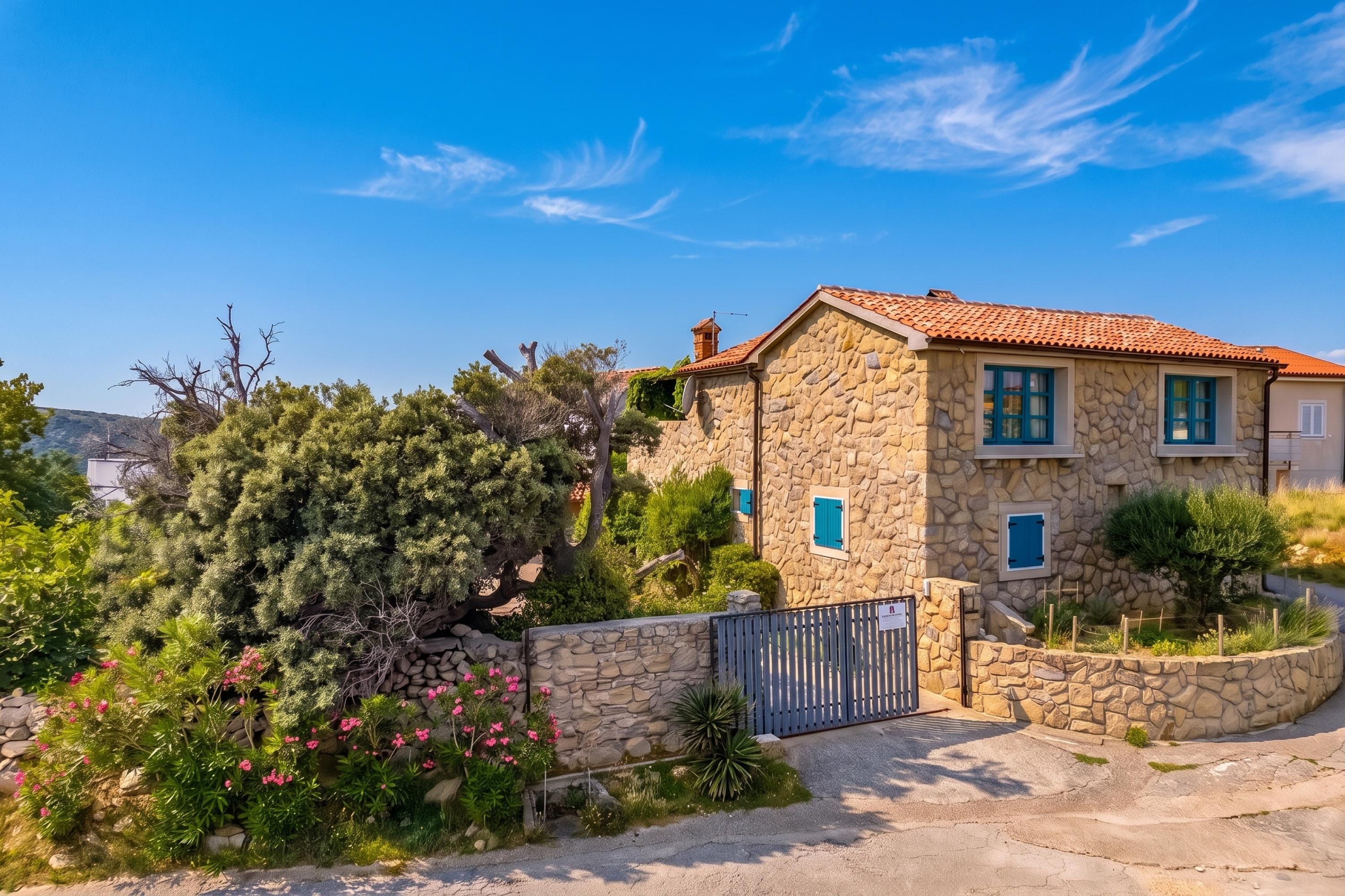 A stone house with a tiled roof, a gated entrance, and a well-maintained garden with various plants and flowers.