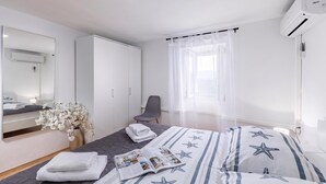 A hotel room with a bed, a chair, a desk, a mirror, a wardrobe, and an air conditioning unit. - Hidden Hill Lopar With Sauna & Jacuzzi (Lopar)