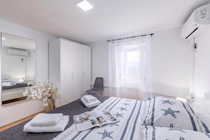 Habitación de hotel con cama, silla, escritorio, espejo, armario y aire acondicionado.
