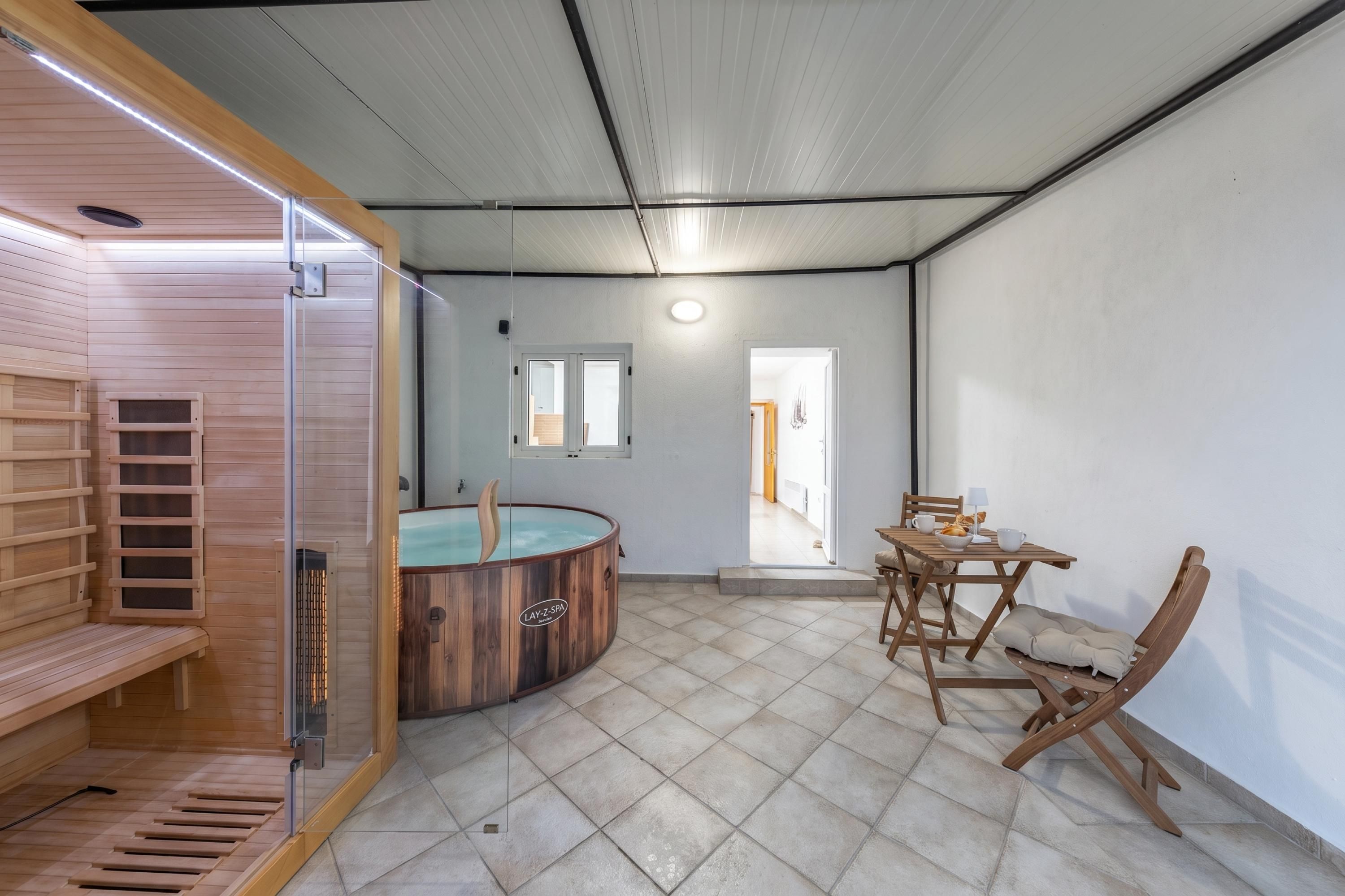 Un cuarto de sauna con un banco de madera, una mesa de madera con sillas y una bañera de hidromasaje con paredes de vidrio.