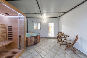 Un cuarto de sauna con un banco de madera, una mesa de madera con sillas y una bañera de hidromasaje con paredes de vidrio.