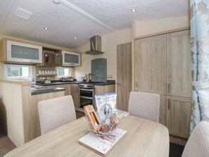 A compact kitchen with a microwave, stove, and sink, a dining area with a table and chairs, and a large wardrobe. - Mallard is situated in Shobdon (Leominster)