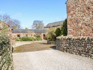 A courtyard with stone walls, a gravel path, and a building with a sloped roof. - Rayson Hall Barns, Ousby (Penrith)