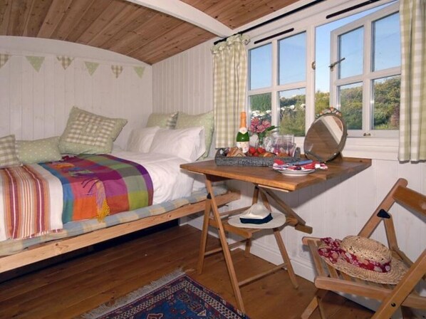 A cozy bedroom with a bed, a wooden desk, a chair, and a window with curtains.