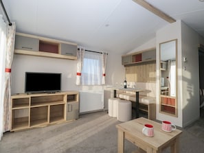 A modern living room with a flat-screen TV, wooden furniture, a dining table with a wine bottle, and a large mirror.